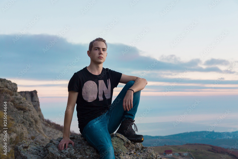 Young attractive man located with on the top of mountains against the backdrop against a blue and pink sunset, looking towards the camera Young attractive man located with on the top of mountains against the backdrop against a blue and pink sunset, looking towards the camera