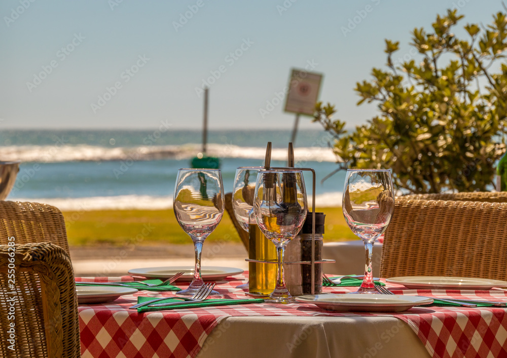 A table with wine glasses at an outdoor cafe with a view of the ocean image with copy space in landscape format