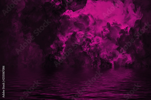 Purple rolling billows of smoke clouds from dry ice across the bottom light with reflection in water.