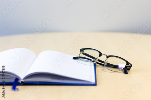 Notebook open with glasses on wooden table , copy space for text.