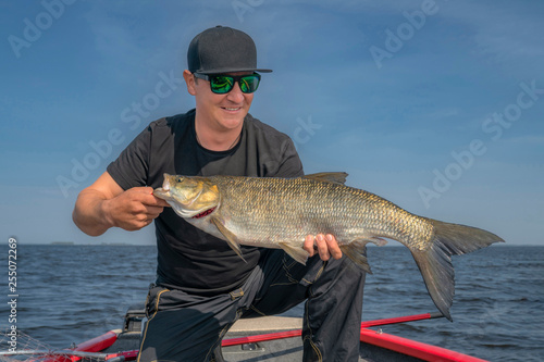 Happy fisherman with big asp fish (aspius) trophy at the boat with fishing tackles