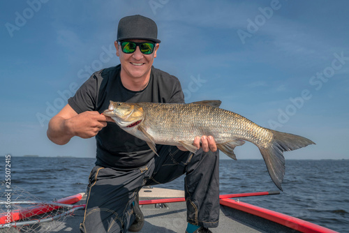 Happy fisherman with big asp fish (aspius) trophy at the boat with fishing tackles