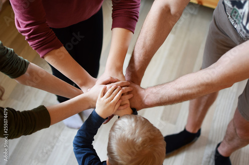 Stack of family people hands - father with children on light brown wooden texture laminate floor background indoors, little boy in middle. Family business, teamwork and unity concept. photo