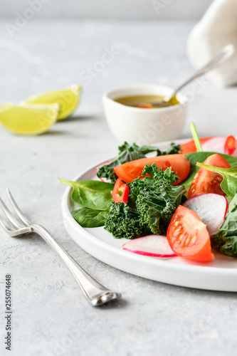 fresh salad of organic spinach, kale, tomatoes and radish with olive oil and lime juice. healthy eating concept. diet, vegan cuisine. light background, selective focus