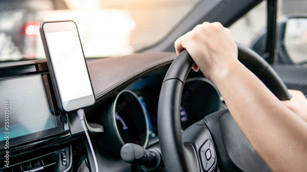 Male driver hand holding on steering wheel using smartphone for GPS navigation. Mobile phone mounting with magnet on the car console in modern car. Urban driving lifestyle with mobile app technology Male driver hand holding on steering wheel using smartphone for GPS navigation. Mobile phone mounting with magnet on the car console in modern car. Urban driving lifestyle with mobile app technology