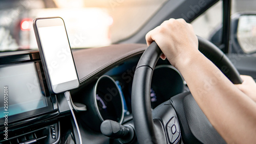 Male driver hand holding on steering wheel using smartphone for GPS navigation. Mobile phone mounting with magnet on the car console in modern car. Urban driving lifestyle with mobile app technology