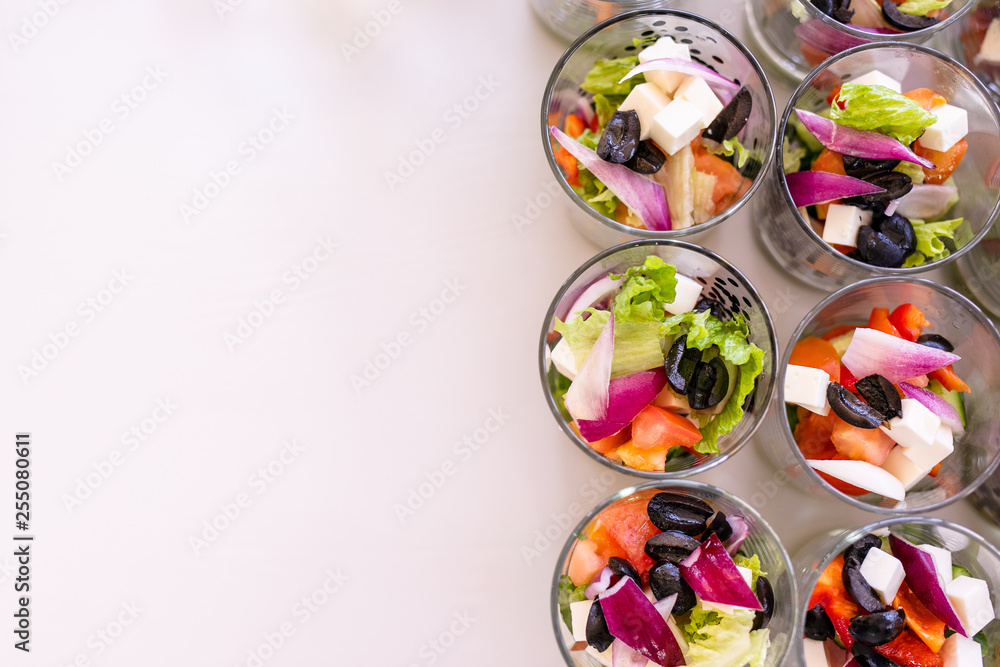 Little glasses with fresh salads, eggs, salmon and cucumbers standing on white table