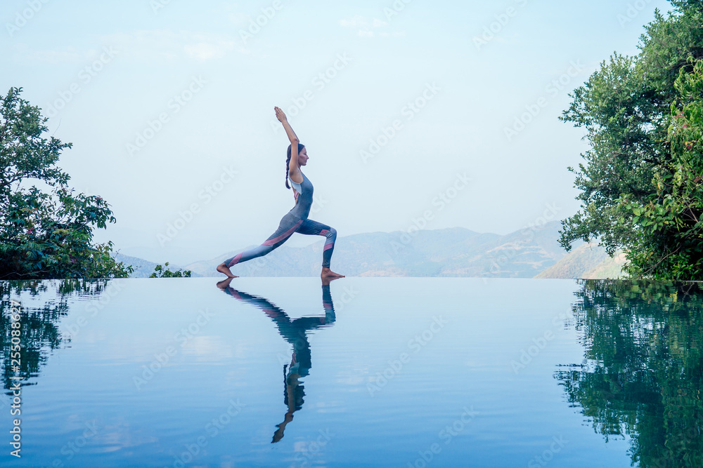 Beautiful woman practice yoga pose on the infinity pool above the mountain peak in the morning in front of beautiful nature views in india goa wildernest nature resorte .romance sunrise in mountains