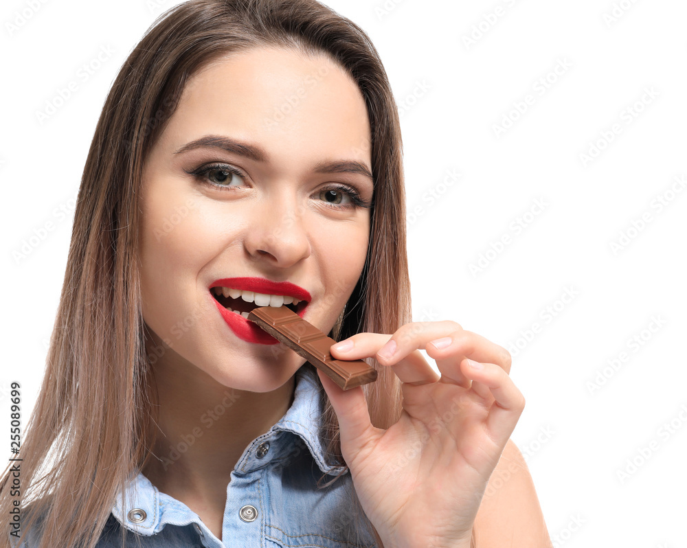 Beautiful young woman eating tasty chocolate on white background