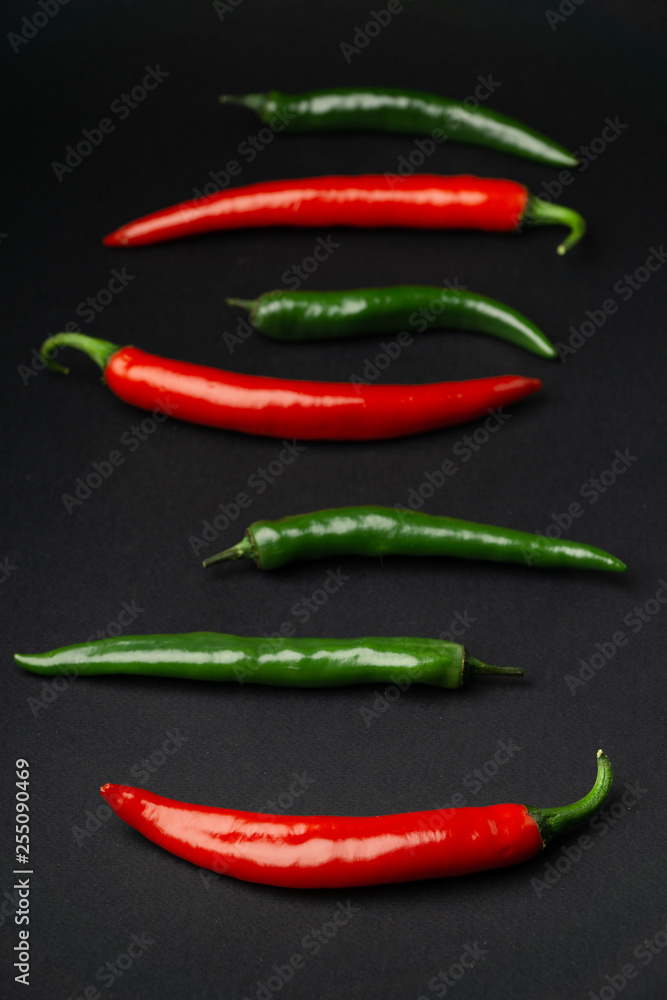 Green and red chili peppers on black background, top view. Hot spicy food symbol.
