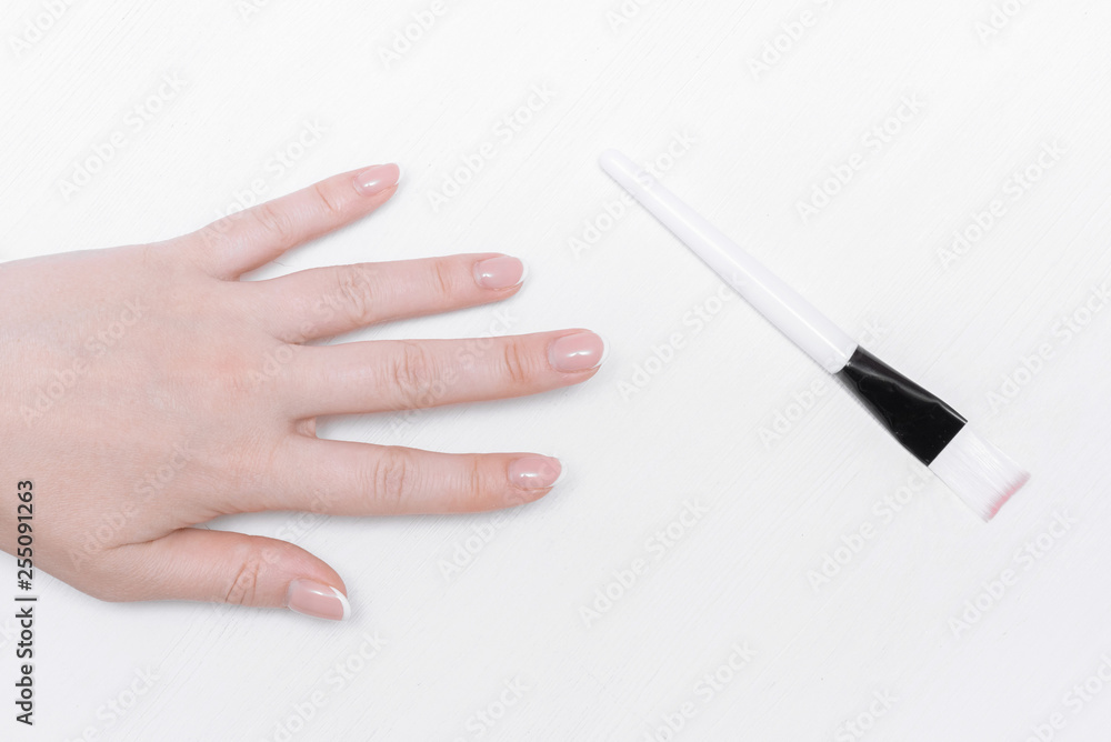 Woman hand is stretching to a makeup brush on the white wooden table background. Woman hand is stretching to a makeup brush on the white wooden table background.