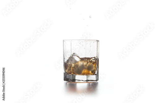 Whiskey splash from the fallen ice cube into glass with beverage on light background..