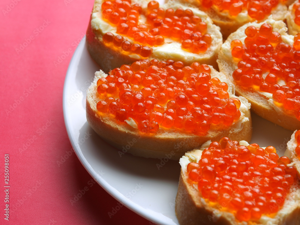 Red caviar on sandwiches in a plate on a pink background.