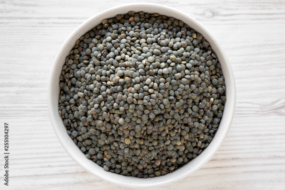 Dry green french lentils in gray bowl over white wooden background, top view. Flat lay, overhead, from above. Close-up. Dry green french lentils in gray bowl over white wooden background, top view. Flat lay, overhead, from above. Close-up.