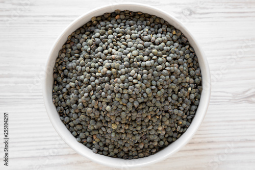 Dry green french lentils in gray bowl over white wooden background, top view. Flat lay, overhead, from above. Close-up.