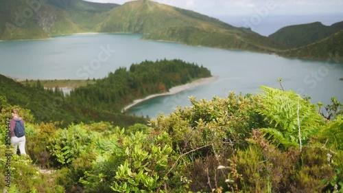 tourist goes down a mountain path in dense vegetation with a beautiful view of the lake in the crater of a volcano