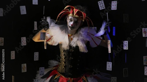 A girl joker with amazing white and black makeup is pushing apart some cards and peeks out photo