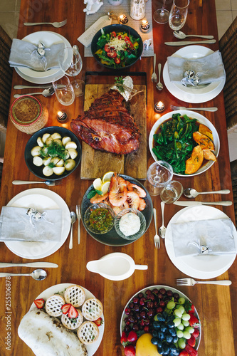 Modern Australian Christmas dinner table with glazed ham, prawns, potatoes and dill, asian greens, Christmas pudding, minced fruit pies by candlelight