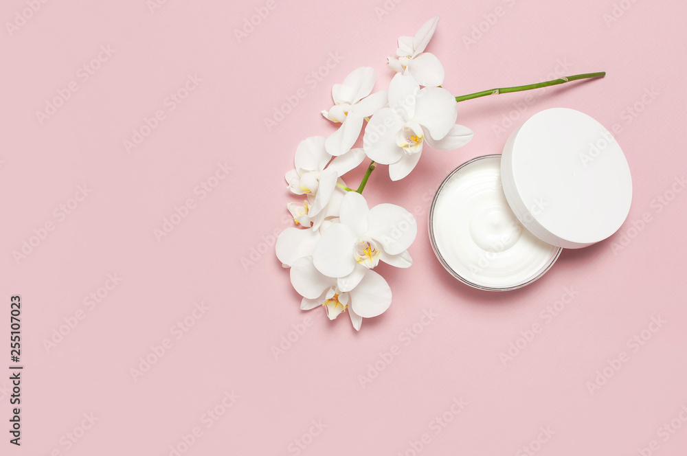 Beauty Spa concept. Opened plastic container with cream and White Phalaenopsis orchid flowers on pink background Flat lay top view. Herbal dermatology cosmetic hygienic cream, organic cosmetic Natural Beauty Spa concept. Opened plastic container with cream and White Phalaenopsis orchid flowers on pink background Flat lay top view. Herbal dermatology cosmetic hygienic cream, organic cosmetic Natural