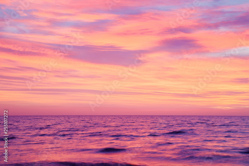 Small, blurry waves of sea and burning purple pink sunset sky. Peaceful atmosphere at beach. Nice nature background. 
