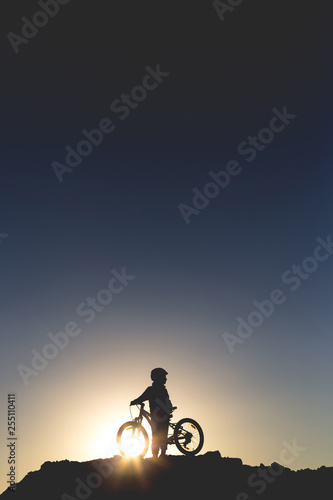 Silhouette of a little girl with a bicycle at sunset