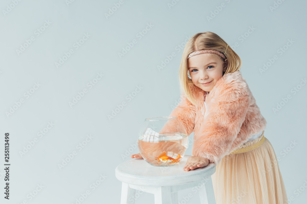 cute kid in faux fur coat and skirt with fishbowl looking at camera isolated on grey cute kid in faux fur coat and skirt with fishbowl looking at camera isolated on grey