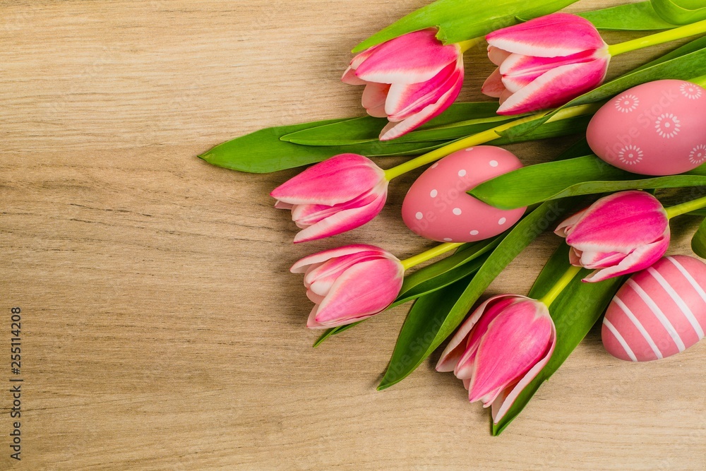 A bunch of fresh pink and white tulip flowers with green leaves and Easter eggs placed on wooden table, copy space, top view, spring flat layout decoration in pastel colors