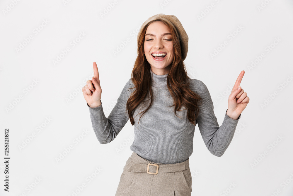 Portrait of joyful woman 30s wearing hat smiling and pointing fingers upward at copyspace Portrait of joyful woman 30s wearing hat smiling and pointing fingers upward at copyspace