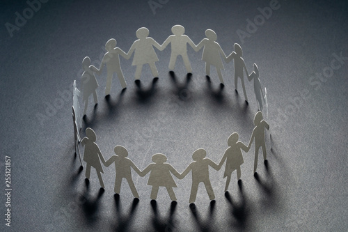 Bild auf Leinwand Circle of paper people holding hands on dark surface