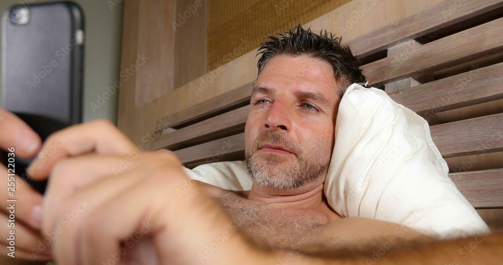 Obraz premium lifestyle portrait young attractive and happy man lying on bed at home bedroom using mobile phone enjoying internet social media app or online gambling and dating