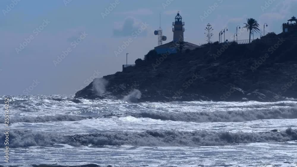 The lighthouse stands on a cliff and the waves of the stormy Mediterranean Sea fall on its rocks The lighthouse stands on a cliff and the waves of the stormy Mediterranean Sea fall on its rocks