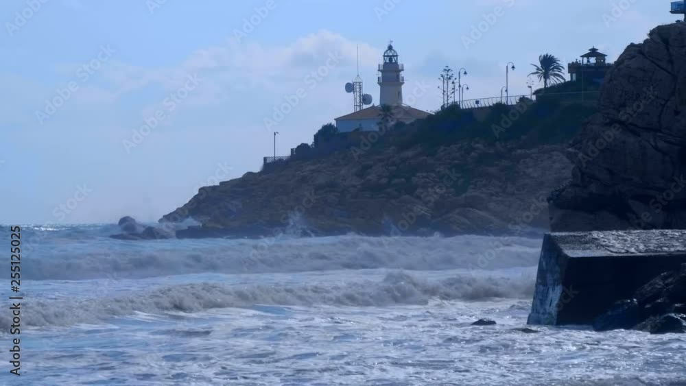 The lighthouse stands on a cliff and the waves of the stormy Mediterranean Sea fall on its rocks The lighthouse stands on a cliff and the waves of the stormy Mediterranean Sea fall on its rocks