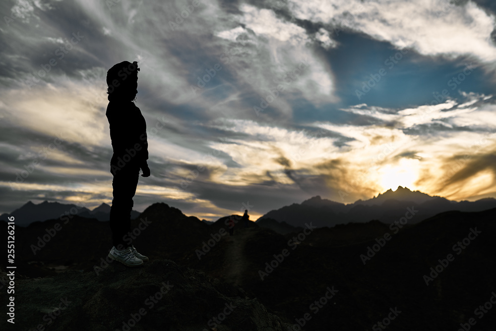 Beautiful sunset with clouds in the mountains at the top of the mountain contour of a standing boy looking towards the sunset