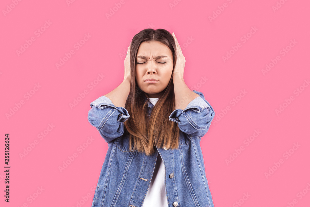 a young girl in a denim jacket covers her ears with her hands on a pink isolated background a young girl in a denim jacket covers her ears with her hands on a pink isolated background