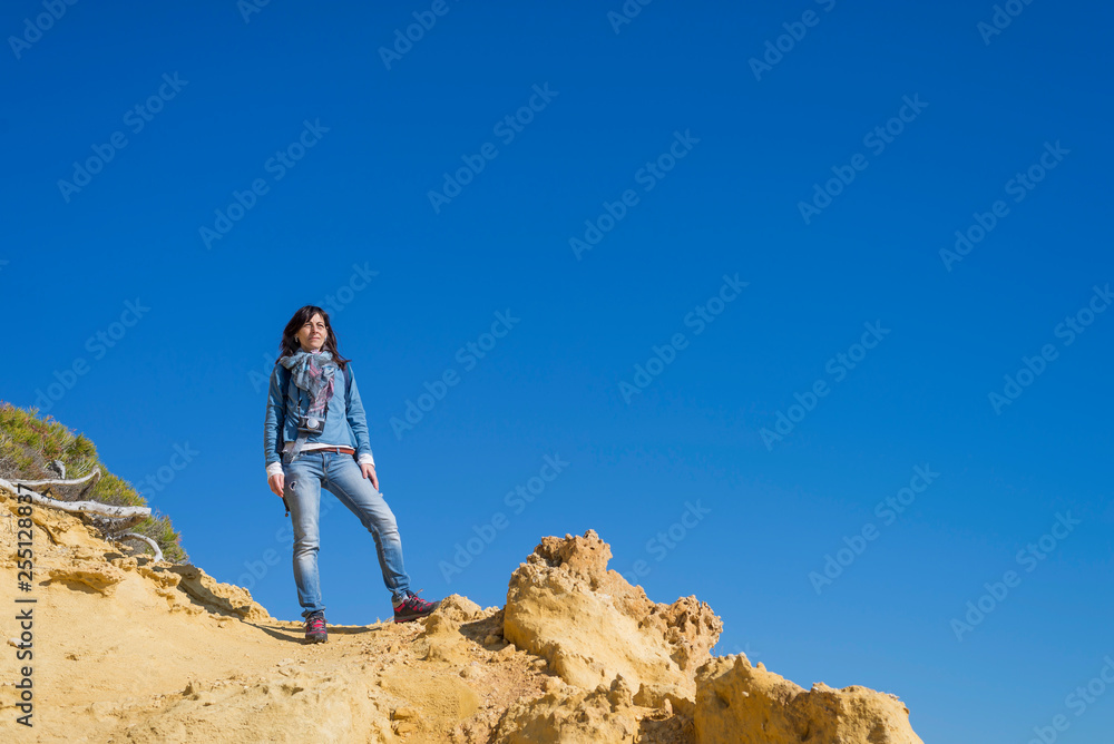 Naklejka premium Widok z boku młodej kobiety ubrane w zwykłe ubrania, stojąc na plaży, patrząc na horyzont w jasny dzień