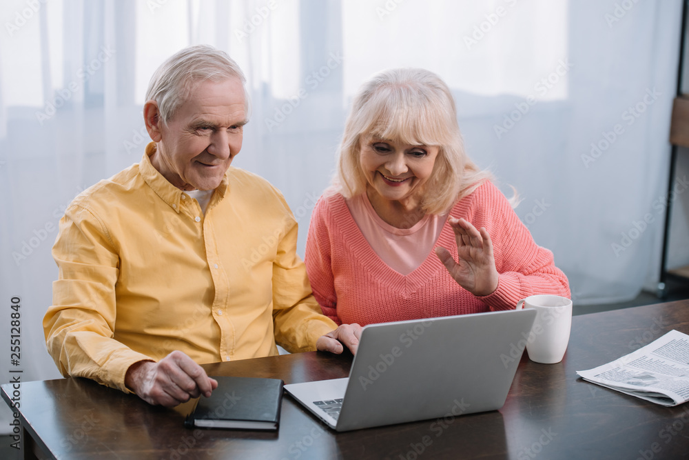 senior couple sitting at table and using laptop during video call at home senior couple sitting at table and using laptop during video call at home