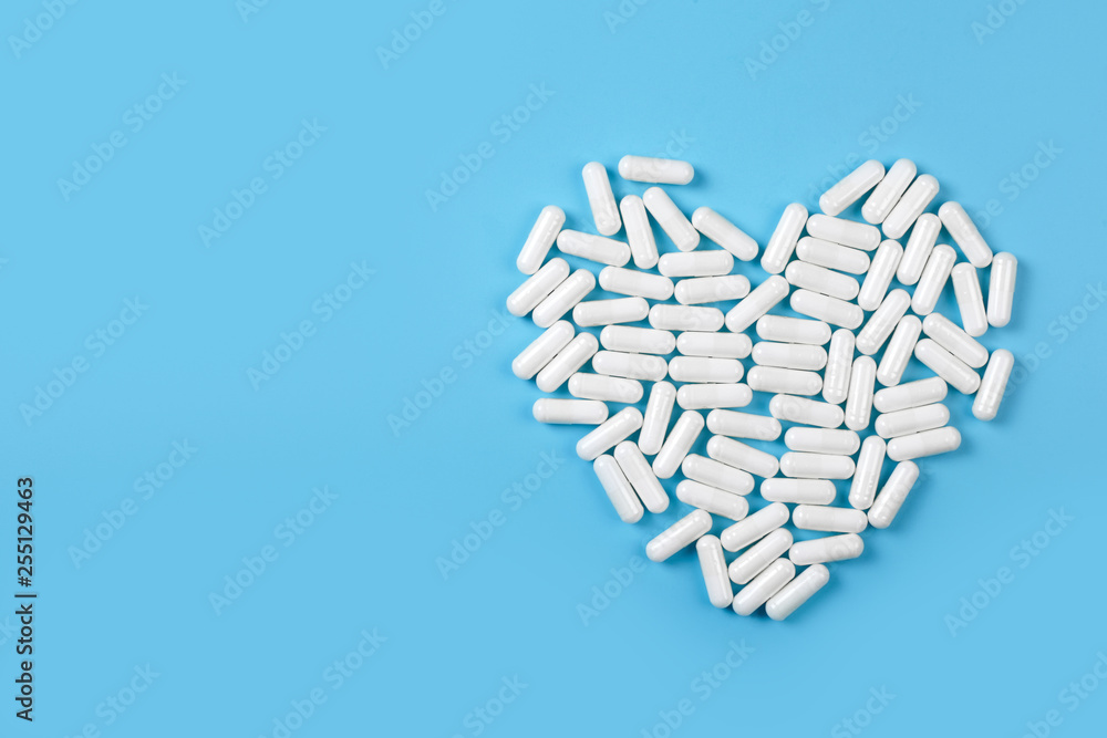 White pills forming heart shape on blue background. Medical care concept.