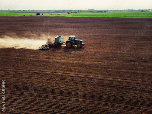Tractor cultivating field, kicking up rocks and dust in early morning