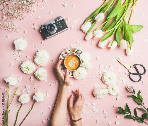 Flat-lay of female hands holding cup of espresso coffee, scissors, film camera, white tulips and buttercup flowers over pink background, top view. Spring or Women's Day holiday concept photo