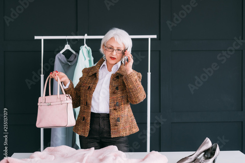 Showroom for VIP. Senior business woman shopping. Aged lady talking on smartphone while choosing new trendy outfit. photo