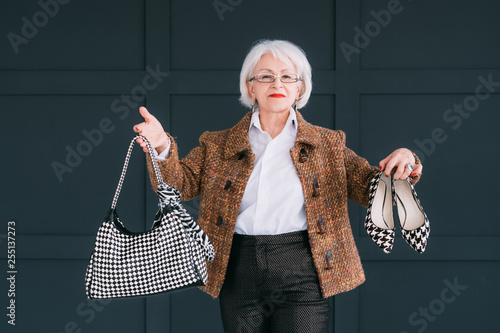 Senior fashion stylist. Personal consultant on trendy wardrobe. Confident aged lady posing with bag and shoes. photo