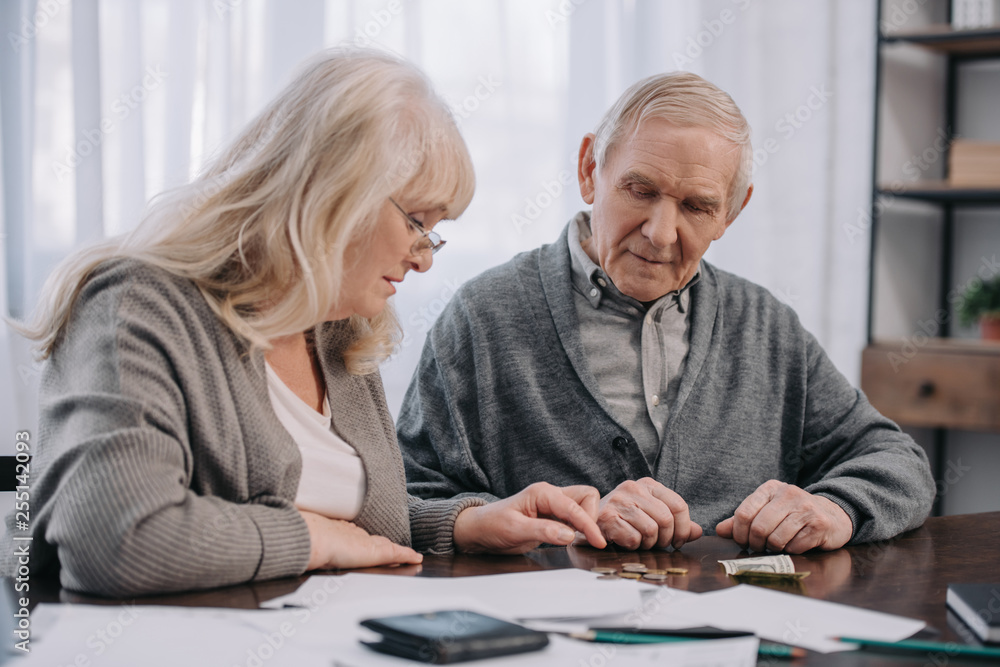 Senior couple in casual clothes sitting at table with paperwork while counting money Senior couple in casual clothes sitting at table with paperwork while counting money