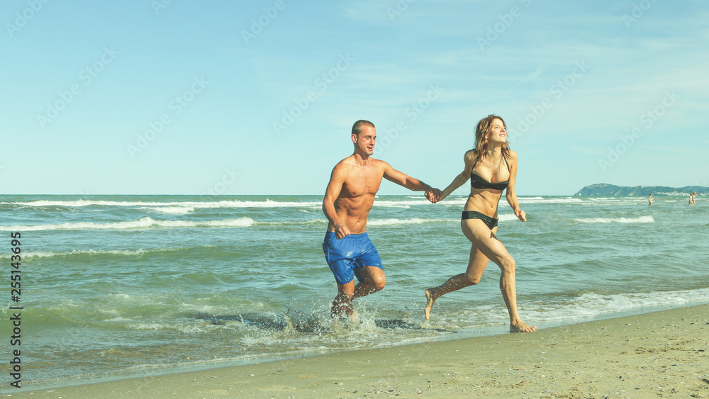 young couple running on beach hand in hand, romantic honeymoon vacation active holiday concept