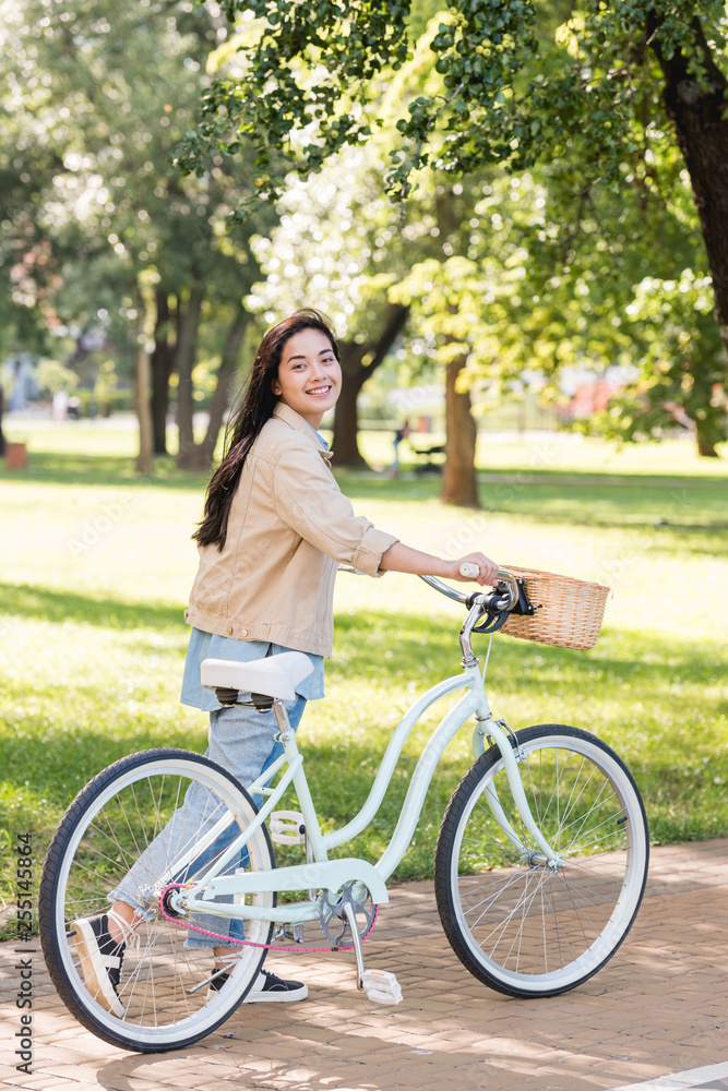 cheerful young woman smiling while riding bicycle in park cheerful young woman smiling while riding bicycle in park