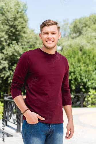 happy young man smiling while standing with hand in pocket