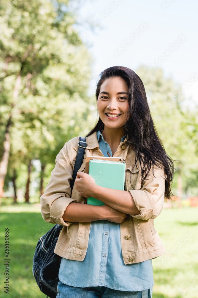 pretty young woman holding books and smiling in park pretty young woman holding books and smiling in park