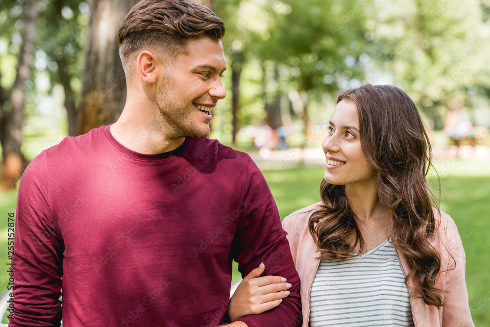 cheerful couple looking at each other while smiling in park