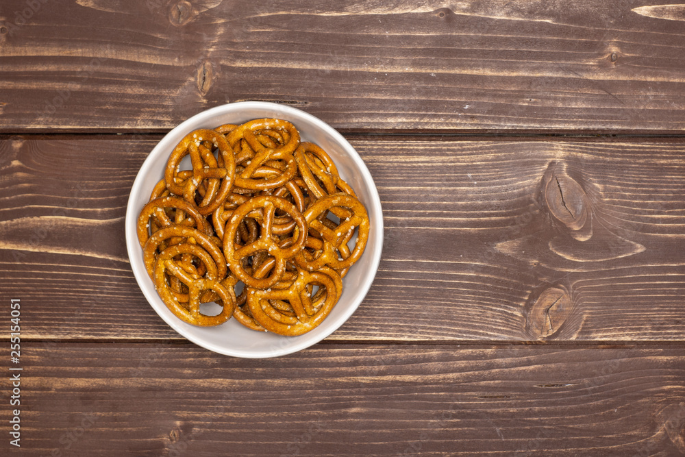 Lot of whole mini salted pretzels in a grey ceramic bowl flatlay on brown wood Lot of whole mini salted pretzels in a grey ceramic bowl flatlay on brown wood