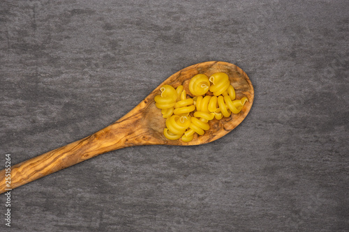 Lot of whole raw pasta funghetto variety in a wooden spoon flatlay on grey stone