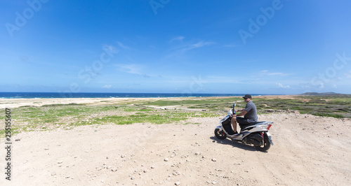 Young man on the Aruba beach on the motorcycle looking on horizon 